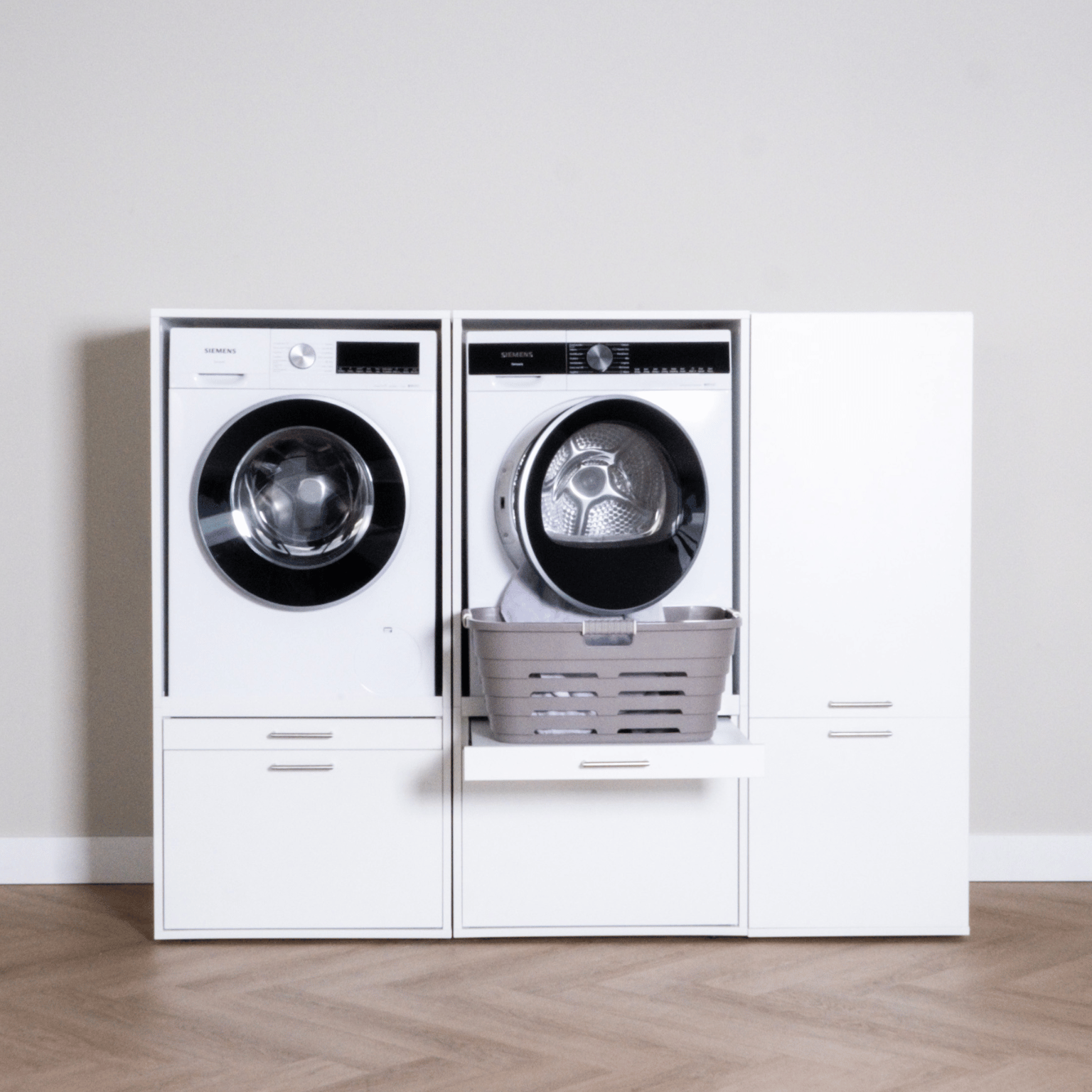 White front-load washer and dryer set with storage cabinets on each side and pull-out drawer with laundry basket in the.