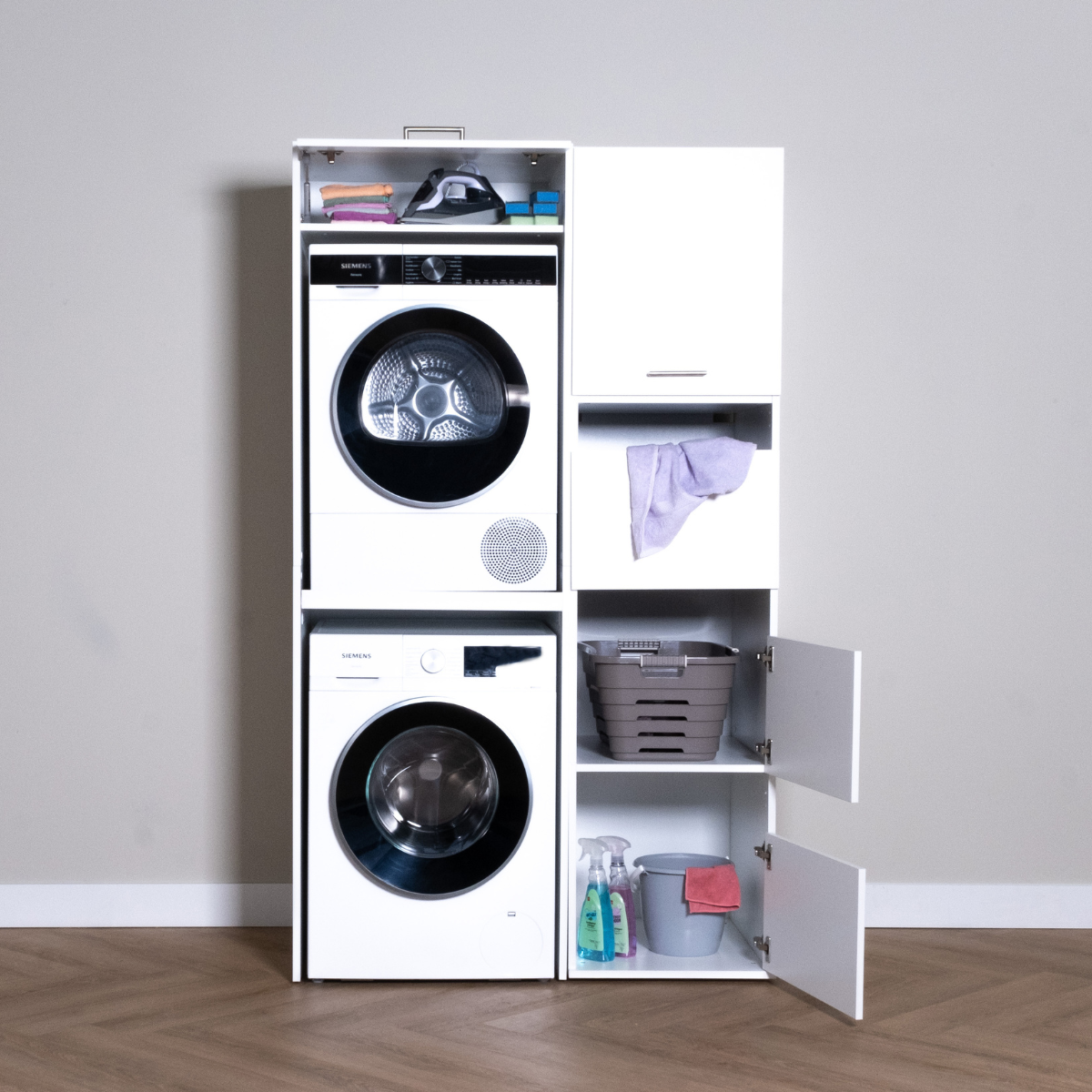 White stacked washer and dryer set with three open storage cabinets and two open shelves against a plain wall.