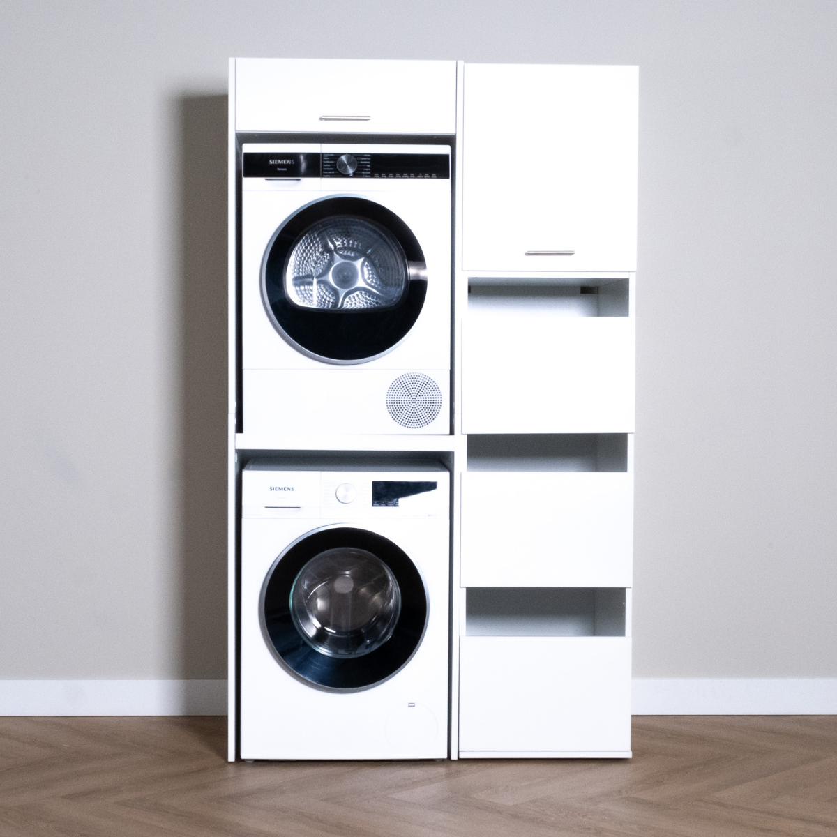 White stacked washer and dryer set with adjacent tall white storage cabinet featuring open shelves and a door.